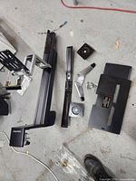 Disassembled Ergotron desk mounting monitor stand parts including arm segments, base clamp, mounting plate, angle bracket, and screws on concrete floor.
