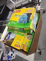 Box containing multiple Glad trash bag boxes and one roll of green trash bags.