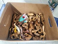 Box filled with multiple handcarved wooden animal napkin rings, showing a variety of shapes and colors.
