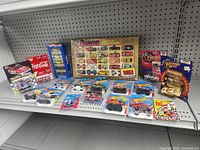 Overall view of the shelf with multiple diecast vehicles and boxed sets including Coca-Cola, Revell, Hot Wheels Ferrari pack, Diamond Wheels set, Winners Circle boxed cars.