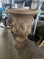 Side view of large plastic flower urn with classical leaf decorations on the body and two rounded handles attached on each side.