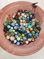 Large pinkish ceramic bowl filled with a mix of colorful glass marbles of various designs and sizes.