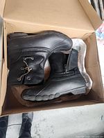 Pair of women's black Sperry boots in cardboard box, soles and upper visible.