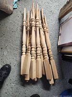 Stack of 17 unpainted wooden spindles arranged on floor showing turned detail and length.