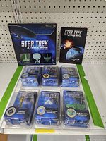Full view of Star Trek Attack Wing Miniatures Game box containing three miniatures visible through window, six additional figures in clamshells, and Rules of Play booklet laid on green surface.