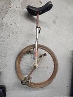 Full view of the unicycle showing single wheel, seat, and pedal. Rust visible on metal parts.