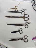 Six vintage snips/scissors of varying sizes and styles laid out on a white surface.