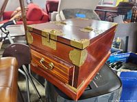 Wooden jewelry box showing brass corner accents and latch, and side drawer with handle.