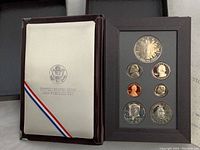 Photo of the 1989 United States Mint Congressional Coin Set showing the silver dollar, half dollar, quarter, nickel, penny, and commemorative bicentennial silver dollar coins mounted in a black presentation frame alongside the protective booklet insert inside the original box.