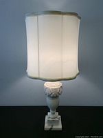 Front view of vintage alabaster lamp illuminated with shade on showing scalloped edge and stone base details.