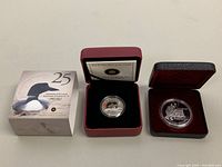 Two silver coins displayed with their original protective boxes, including an outer cardboard box for the 2012 coin.
