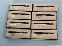 Overview of eight black CROSS ballpoint pens in their cushioned display cases arranged in two rows of four.