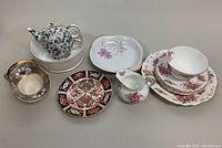 Assorted chinaware displayed including teapot, plates, and creamer and sugar bowl set, showing overall lot contents and condition