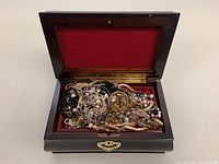 Closed dark wooden jewelry box with red velvet interior containing assorted tangled jewelry