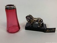 Photo showing cranberry glass sugar shaker with sterling silver band and Ben-Zion lion sculpture on black base with tag.