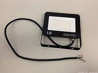 Single black LED floodlight with a mounting bracket and wire with exposed ends, laying on a white surface.