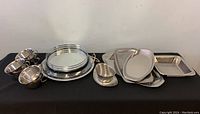 Full view of all the stainless steel servingware items arranged in a line on a black surface showing different shapes and sizes.