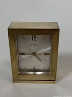 Front view of the Swiza brass alarm clock displaying the rectangular brass housing and clock face with hands.