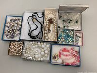 Overview of the vintage assorted costume jewelry including multiple beaded necklaces and earrings in small boxes arranged on a surface.