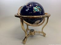 Side angle view of the vintage globe showing natural stone inlays and gold stand with compass