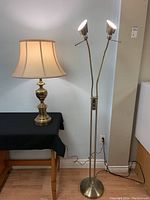 Side-by-side view of the vintage brass table lamp with fabric shade and the dual-headed brass floor lamp, both turned on, showing overall condition and lighting.