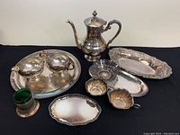 Full lot overview showing silver plated teapot, trays, bowls, and green glass cup with silver holder.