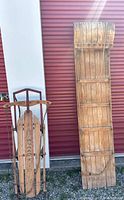 Front view of Speed King sled next to wooden toboggan showing overall shape and condition.