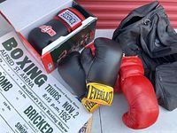 Red Pollack boxing gloves, black Everlast gloves with yellow logo, Ringside gloves in box, black gym bag and boxing promotional poster shown on surface.