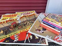 Several colorful promotional circus posters including Cole Brothers, Murray Brothers, and others. Also a ceramic clown figurine and a small circus coach toy displayed on posters.