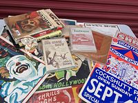 Overview of multiple vintage circus posters and advertising including signage for Shrine Circus, Greater Exposition Shows, and Kelly Miller Circus. Several circus books and magazines visible as a stack on the side, also includes an old ticket sign for Cockshutt Park.