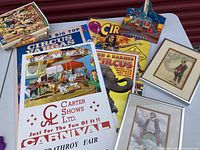 Collection of colorful circus posters, circus books, and framed clown prints arranged on a table.