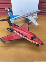 Two vintage tin airplanes: red Tonka friction plane and silver Overseas Air Lines ST-1 airplane displayed on a wooden surface.