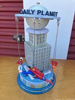 Front angle showing Superman figure flying horizontally in front of building model with Daily Planet globe and circular top plate with lettering.