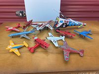Wide shot capturing all tin and metal airplanes spread out on wooden surface with police helicopter in back.