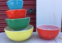 Stacked view of four Pyrex colored mixing bowls in descending size order: yellow, green, orange, blue. Next to them is a separate orange bowl.