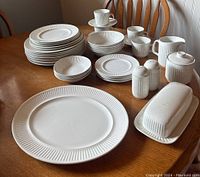 Full set displayed on wooden table showing all items including plates, bowls, cups, saucers, cream and sugar, butter dish, salt and pepper shakers, serving platter.
