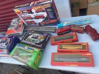 Photo showing boxed Lionel Heartland Classic train set, boxed Hornby Canadian Pacific smoking car, boxed Hornby train carriages, boxed tiny wind-up train, loose train set parts, and assorted train-related items on white table.