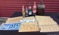 Photo showing three bottles (NuGrape, Wishing Well, Coca-Cola) and several stacked Ontario licence plates with visible years and rust.