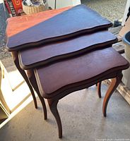 Three solid wood nesting tables stacked showing scalloped edges and leg style.