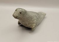 Front view of a small gray stone seal carving on white background, showing seal's face and flipper details.