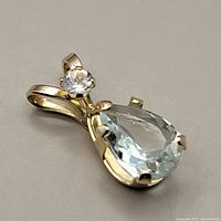 Close-up front angle of the 10K gold pendant showing pear-shaped aquamarine and round moonstone set in prongs.