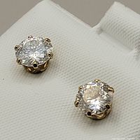 Close-up photo of the gold stud earrings with large round moissanite stones mounted on a white display.