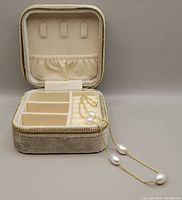 Open velvet travel box showing cream interior compartments and necklace draped inside
