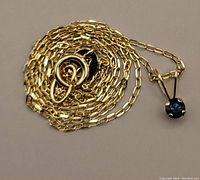 Coiled yellow gold chain with sapphire pendant visible at right edge