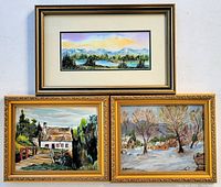 Three framed paintings grouped. Top is watercolor lake scene with mat and glass. Bottom left is watercolor rural house and greenery. Bottom right is oil painting of winter village scene. All framed in vintage wood frames.