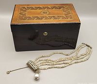 Photo showing the wooden box with geometric inlay lid alongside the pearl tone bracelet, both items in the lot.
