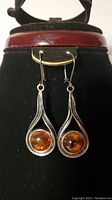 Front view of the pair of amber and sterling silver drop earrings hanging from a stand, showing the round amber stones set in silver teardrop frames.