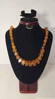 Full view of amber faceted bead necklace displayed on a black jewelry stand, showing graduated size of beads.