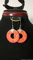 Front view of coral and sterling silver drop earrings hanging on black display stand showing circular coral pendants and silver grape motif detail.