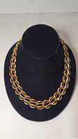 Front view of the gold-colored large link necklace displayed on a black bust stand showing overall design and length.